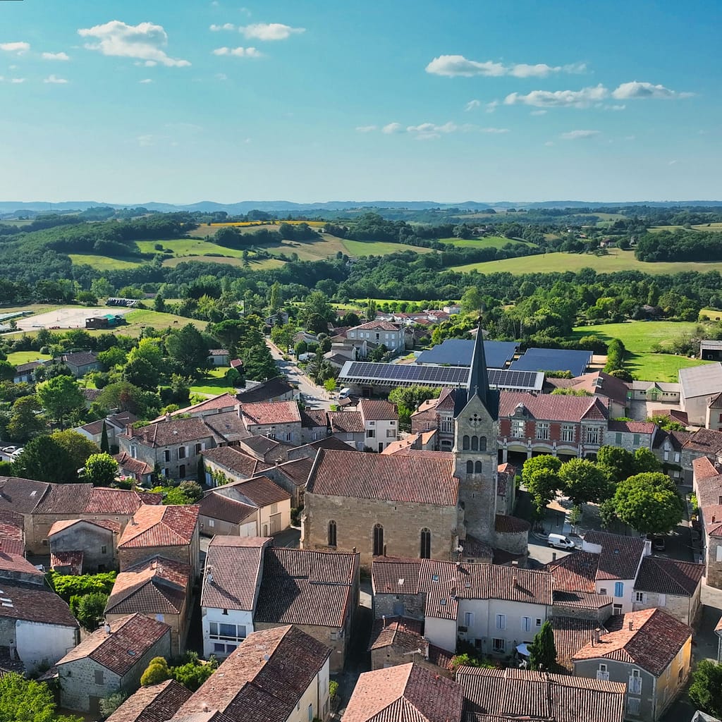 Vue aérienne de la cité historique de Prayssas dans un paysage de collines avec un ciel bleu